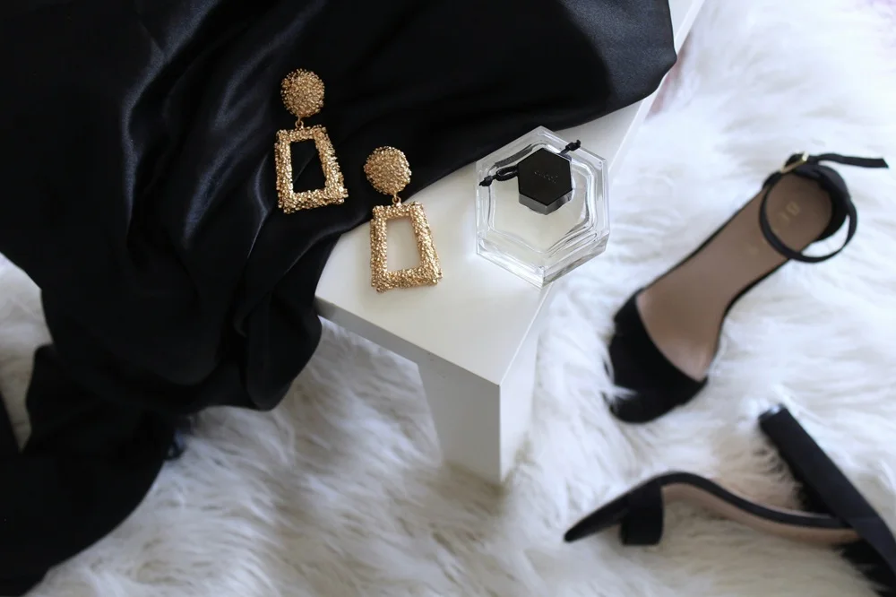 Black fashion accessories, gold earrings and heels arranged in a luxury editorial still life